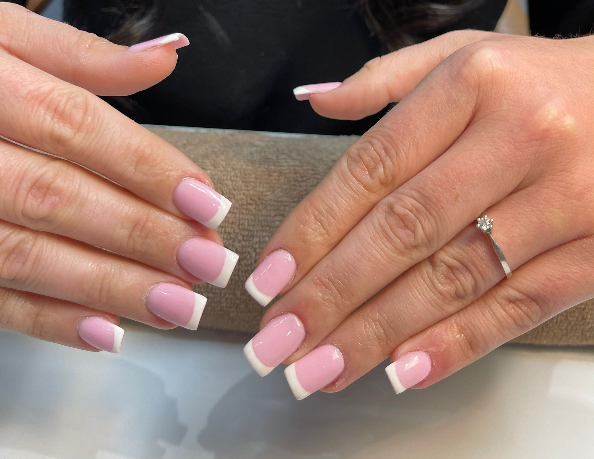 Roze French nagels met witte tips, op een grijs kussen